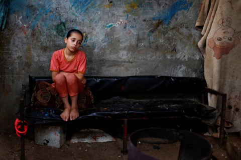 Seorang gadis Palestina duduk di dalam rumah keluarganya di tengah gelombang panas dan pemadaman listrik yang panjang di Kota Gaza, Palestina, Senin (1/8/2022). Foto: Mohammed Salem/REUTERS