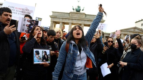 Seorang demonstran memegang rambutnya yang telah dipotong selama aksi protes menyusul kematian Mahsa Amini, di depan Gerbang Brandenburg di Berlin, Jerman, Jumat (23/9/2022). Foto: Christian Mang/REUTERS