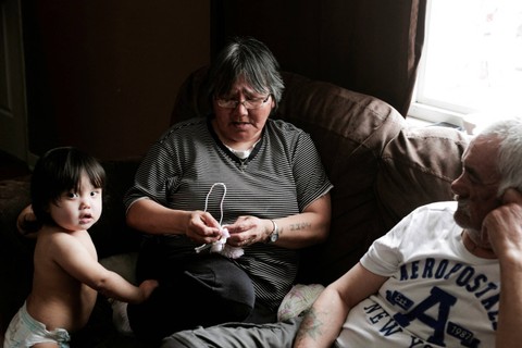 Katie Winters (54) merajut topi tradisional untuk Paskah sementara suaminya Sonny Winters (64) mengawasi cucunya Tony Tsakapesh (1) di rumah mereka di Nain, Newfoundland dan Labrador, Kanada, Jumat (15/4/2022). Foto: Melissa Renwick/Reuters