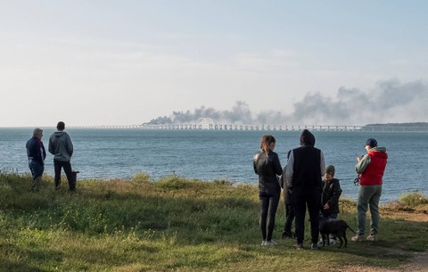 Orang-orang menyaksikan tangki bahan bakar terbakar dan merusak bagian jembatan Kerch di Selat Kerch, Krimea, Sabtu (8/10/2022). Foto: Stringer/Reuters