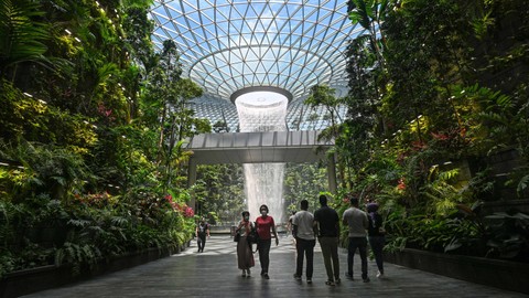 Orang-orang berjalan melewati fitur air terjun dalam ruangan Rain Vortex di Bandara Jewel Changi di Singapura. Foto: AFP/Roslan Rahman