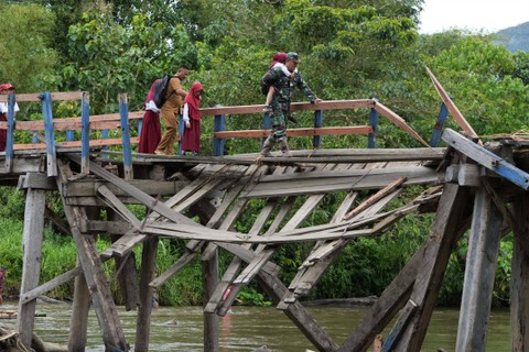Seorang guru bersama Babinsa TNI AD membantu sejumlah siswa SD Negeri 1 Alaaha saat menyeberangi jembatan rusak di Desa Alaaha, Kecamatan Ueesai, Kolaka Timur, Sulawesi Tenggara, Sabtu (21/1/2023). Foto: Jojon/Antara Foto