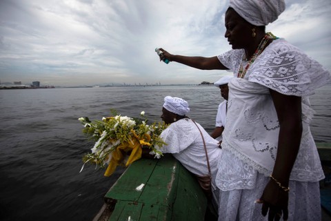 Seorang pemuja dewi laut Yemanja menempatkan bunga persembahan untuknya di perairan pantai Diabo selama perayaan tahunan dewa tersebut, di Rio de Janeiro, Brasil, Kamis (2/2/2023). Foto: Bruna Prado/AP Photo