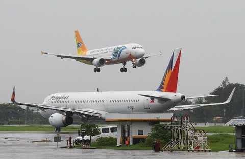 Ilustrasi - Pesawat Cebu Pacific Airlines (atas) bersiap untuk mendarat melewati pesawat Philippine Airlines (PAL) (kanan) di Bandara Internasional Manila. Foto: Ted ALJIBE / AFP
