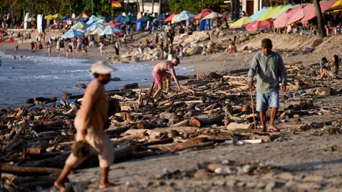 Turis lokal dan mancanegara berjalan diantara puing-puing dan sampah yang terdampar di pantai Kuta di pulau resor Bali, Indonesia pada 18 Februari 2023. Foto: Sonny Tumbelaka/AFP