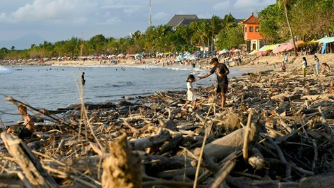 Pengunjung berjalan diantara puing-puing dan sampah yang terdampar di pantai Kuta di pulau resor Bali, Indonesia pada 18 Februari 2023. Foto: Sonny Tumbelaka/AFP