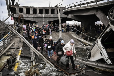 Warga menyebrangi jembatan yang hancur selama invasi Rusia ke eilayah Ukraina di wilayah kota Irpin, pada 5 Maret 2022. Foto: Aris Messinis/AFP