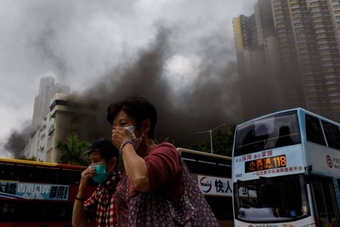 Orang-orang menutupi hidung mereka saat kepulan asap terlihat di sebuah gudang yang terbakar, di distrik Kowloon yang ramai di kota itu, di Hong Kong, China, Jumat (24/3/2023). Foto: Tyrone Siu/REUTERS