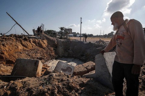 Warga Palestina memeriksa lokasi serangan udara yang menargetkan situs militer di Deir al Balah di Jalur Gaza tengah, usai serangan udara dari Israel, pada Rabu (3/5/2023). Foto: Anas Baba/AFP