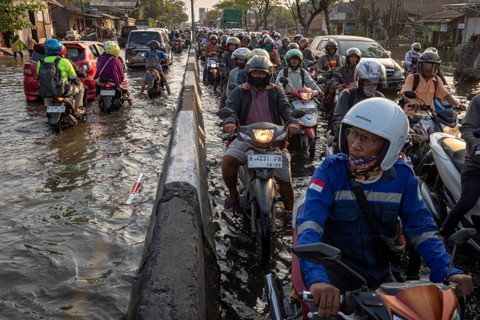 Pengendara sepeda motor melaju perlahan saat menembus genangan air rob (limpasan kenaikan air laut ke daratan) di jalur Pantura Demak KM 10, di Kecamatan Sayung, Kabupaten Demak, Jawa Tengah, Sabtu (13/5/2023). Foto: Aji Styawan/ANTARA FOTO