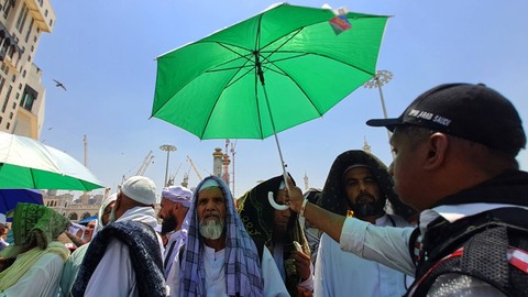 Seorang petugas PPIH Arab Saudi memayungi jamaah saat menunggu dibukanya jalan menuju terminal Bir Ali di Mekah, Arab Saudi, Selasa (6/6/2023). Foto: ANTARA FOTO/Wahyu Putro A