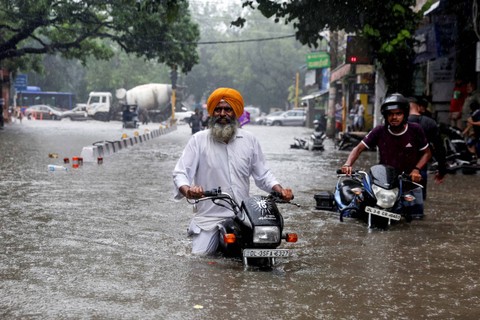 Seorang pria dengan sepeda motornya mengarungi jalan yang banjir setelah hujan lebat di New Delhi, India, India, Sabtu (8/7/2023). Foto: Anushree Fadnavis/REUTERS