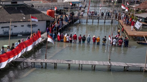 Warga mengikuti upacara bendera di perkampungan mereka yang terendam limpasan air laut ke daratan atau banjir rob di Dusun Timbulsloko, Desa Timbulsloko, Kecamatan Sayung, Kabupaten Demak, Jawa Tengah, Kamis (17/8/2023). Foto: Aji Styawan/Antara Foto