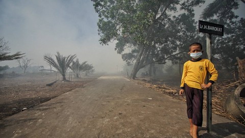 Seorang anak kecil yang mengenakan masker pelindung saat kabut asap menyelimuti perkampungan di Palembang, Minggu (17/9) Foto: abp/urban id