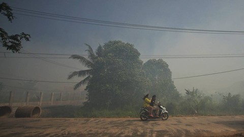 Dua orang warga yang melewati kabut asap yang menyelimuti akses jalan di perkmapungan di Palembang, Minggu (17/9) Foto: abp/urban id