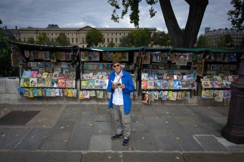 Alain Papillaud, "bouquiniste" berusia 74 tahun berpose di depan stannya, tempat ia menjual buku-buku antik dan poster-poster tua, di tepi kiri Sungai Seine di Paris pada 29 Agustus 2023. Foto: Miguel MEDINA / AFP
