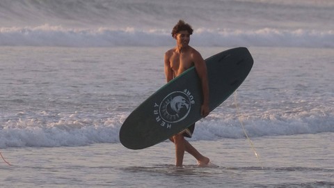 Wisatawan membawa papan selancar berjalan menuju ke tengah laut saat berlibur di Pantai Kuta, Badung, Bali, Senin (25/9/2023). Foto: Nyoman Hendra Wibowo/Antara Foto