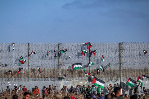 Bendera Palestina dipasang di pagar kawat berduri saat demonstrasi 'pawai bendera' di sepanjang perbatasan dengan Israel di sebelah timur kota Gaza pada 18 Mei 2023. Foto: Mohammed Abed/AFP