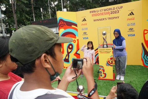 Pengunjung berfoto bersama trofi Piala Dunia U-17 di Bundaran HI, Jakarta, Minggu (15/10/2023). Foto: Iqbal Firdaus/kumparan