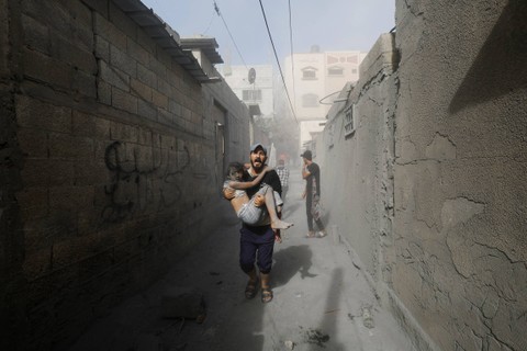 Seorang pria Palestina membawa korban anak-anak di lokasi serangan Israel terhadap rumah-rumah, di Khan Younis di Jalur Gaza selatan, Kamis (26/10/2023). Foto: Mohammed Salem/REUTERS