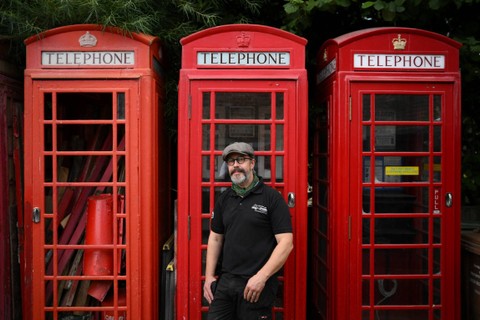 Pemilik Carl Burge, berpose di depan bilik telepon tradisional berwarna merah di "Remember When UK", sebuah perusahaan yang mengkhususkan diri dalam restorasi memorabilia Inggris di King's Lynn, di timur Inggris. Foto: Daniel LEAL/AFP