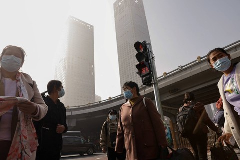 Orang-orang yang memakai masker menunggu di persimpangan di Kawasan Pusat Bisnis (CBD) Beijing, saat kota itu diselimuti kabut asap, di China, Rabu (1/11/2023). Foto: Tingshu Wang/REUTERS