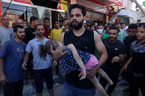 Seorang pria membawa seorang gadis muda yang terluka ketika sebuah supermarket terkena serangan Israel di kamp pengungsi Rafah di Jalur Gaza selatan pada 25 Oktober 2023. Foto: Said Khatib/AFP
