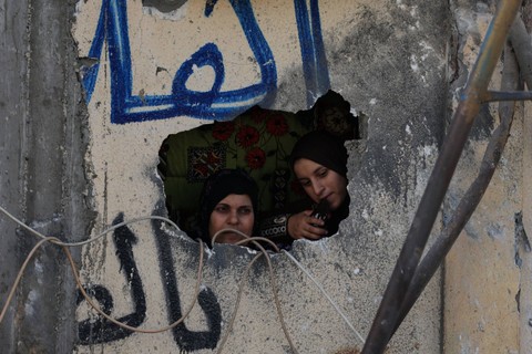 Wanita Palestina melihat keluar dari lubang di tembok yang rusak usai serangan Israel di kamp pengungsi Rafah di Jalur Gaza selatan pada 25 Oktober 2023. Foto: Said Khatib/AFP
