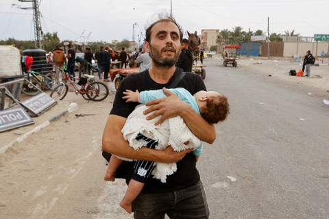 Seorang pria Palestina yang menggendong seorang anak melarikan diri dari Gaza utara saat mereka bergerak ke selatan, Minggu (12/11/2023). Foto: Ibraheem Abu Mustafa/REUTERS