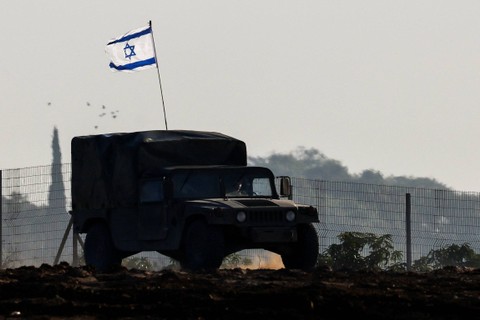 Bendera Israel terlihat di kendaraan militer saat melewati perbatasan Israel setelah meninggalkan Gaza selama gencatan senjata sementara antara kelompok Islam Palestina Hamas dan Israel, di Israel, Jumat (24/11/2023). Foto: Amir Cohen/REUTERS