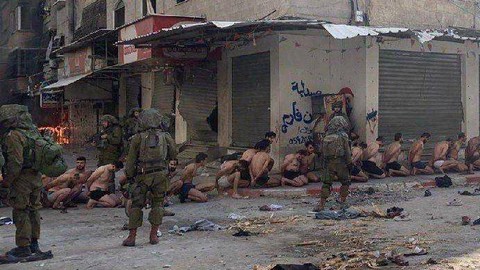 Warga Palestina yang ditangkap dan ditahan duduk di jalan di Beit Lahia, utara Jalur Gaza, sementara tentara Israel berjaga di tengah operasi darat yang sedang berlangsung oleh tentara Israel melawan Hamas, pada Jumat (8/12/2023). Foto: Reuters