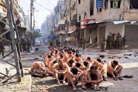 Warga Palestina yang ditangkap dan ditahan duduk di jalan di Beit Lahia, utara Jalur Gaza, sementara tentara Israel berjaga di tengah operasi darat yang sedang berlangsung oleh tentara Israel melawan Hamas, pada Jumat (8/12/2023). Foto: Reuters