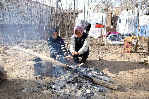 Warga menghangatkan diri di dekat api unggun di samping tenda darurat di desa Sibuzi, Jishishan, provinsi Gansu, China, Rabu (20/12/2023). Foto: Xiaoyu Yin/REUTERS