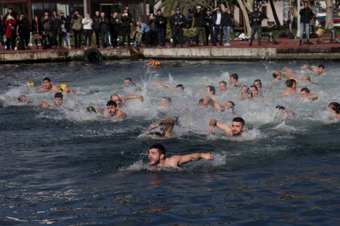 Umat Ortodoks Yunani berenang di Tanduk Emas untuk menangkap salib kayu yang dilemparkan oleh Patriark Ekumenis Bartholomew I (tidak digambarkan) saat perayaan Hari Epiphany di Istanbul, Turki, Sabtu (6/1/2024). Foto: Murad Sezer/REUTERS