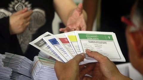 Petugas KPPS menyerahkan kertas suara kepada pemiih di salah satu TPS di Kota Manado.