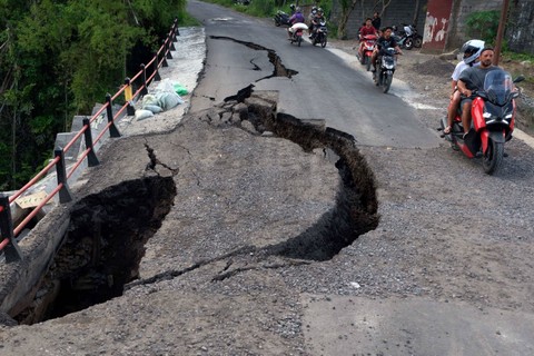 Wisatawan mancanegara dan warga mengendarai sepeda motor melintasi jalan yang ambrol di Desa Taman Bali, Bangli, Bali, Minggu (18/2/2024). Foto: Nyoman Hendra Wibowo/Antara Foto