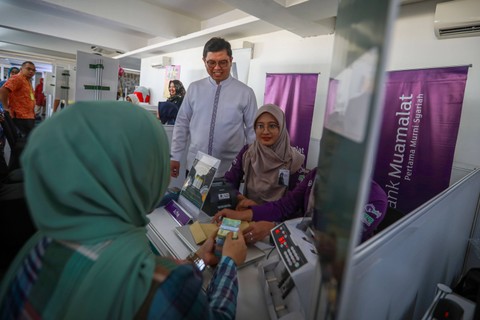 Direktur Utama PT Bank Muamalat Indonesia Tbk Indra Falatehan dibantu petugas teller bank melayani warga di lokasi penukaran uang Rupiah pada momen Ramadan dan Idulfitri 2024 di Istrora Senayan, Jakarta, Kamis (28/3/2024). Foto: Aditia Noviansyah/kumparan