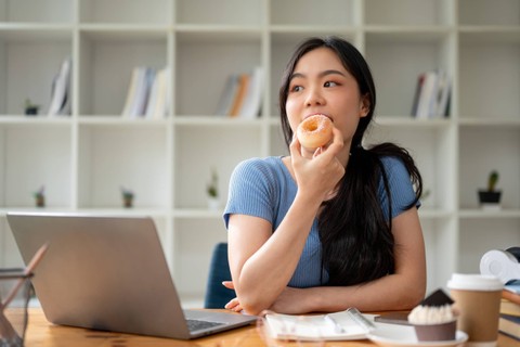 Ilustrasi perempuan makan donat atau makanan manis. Foto: BongkarnGraphic/Shutterstock