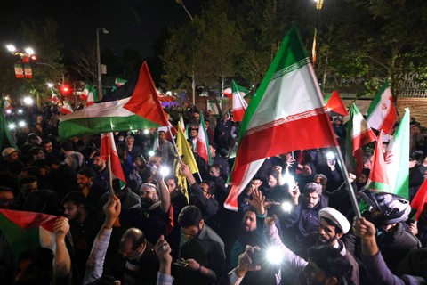 Demonstran mengibarkan bendera Iran saat mereka berkumpul di depan Kedutaan Besar Inggris di Teheran, Minggu (14/4/2024). Foto: ATTA KENARE / AFP