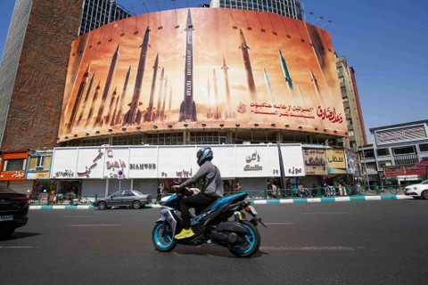 Seorang pria mengendarai sepeda motor melewati papan reklame bergambar rudal balistik Iran yang bertugas di Teheran, Jumat (19/4/2024) Foto: AFP