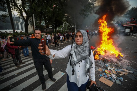 Massa 01 berswafoto dengan latar belakang api saat aksi unjuk rasa di Patung Kuda, Jakarta Pusat, Jumat (19/4/2024) Foto: Aditia Noviansyah/kumparan