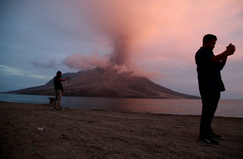 Dua orang jurnalis mengabarkan kondisi Gunung Ruang saat erupsi terlihat dari Pelabuhan Tagulandang, Kabupaten Kepulauan Sitaro, Sulawesi Utara, Rabu (1/5/2024). Foto: Andri Saputra/ ANTARA FOTO