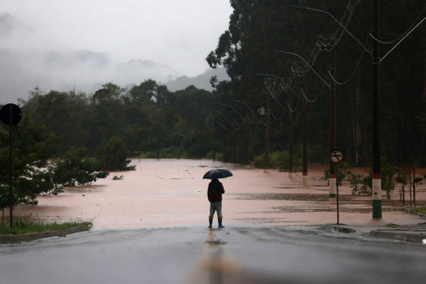 Seorang pria berdiri di depan jalan yang banjir dekat Sungai Taquari saat hujan lebat di kota Encantado di Rio Grande do Sul, Brasil (1/5/2024). Foto: Diego Vara/Reuters