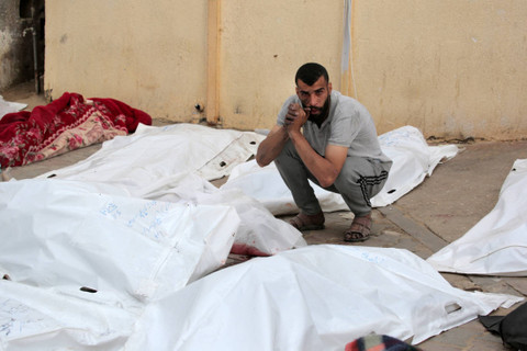 Seorang pria Palestina duduk di dekat mayat orang-orang yang tewas dalam pemboman Israel, di halaman Rumah Sakit Martir Al-Aqsa di Deir al-Balah di Jalur Gaza tengah pada Sabtu (11/5/2024). Foto: AFP