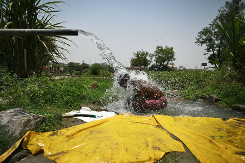 Seorang pria mandi di bawah air yang mengalir dari pipa di sepanjang dataran banjir Yamuna pada suatu sore musim panas yang terik di New Delhi (29/5/2024). Foto: Priyanshu Singh/REUTERS