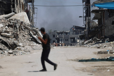 Seorang warga berjalan saat asap mengepul selama serangan Israel di distrik Shujaiya, Kota Gaza pada 28 Juni 2024. Foto: OMAR AL-QATTAA/AFP
