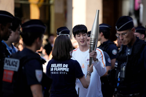 Jin BTS membawa obor Olimpiade 2024 di area Museum Louvre, Paris, Minggu (14/7/2024). Foto: Louise Delmotte/AP