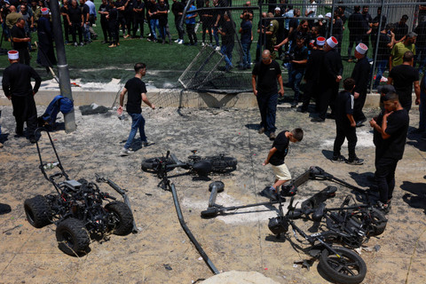 Anggota komunitas Druze melihat pagar yang rusak dan benda-benda yang berserakan di lapangan sepak bola, akibat serangan (28/7/2024). Foto: MENAHEM KAHANA / AFP