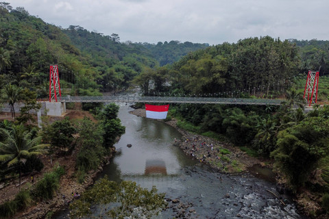 Foto udara warga RW 07 mengibarkan bendera merah putih pada gladi bersih upacara HUT ke-79 Kemerdekaan RI di Jembatan Gantung Sukamenak, Kampung Benteng, Kecamatan Purbaratu, Kota Tasikmalaya, Jawa Barat, Minggu (11/8/2024). Foto: Adeng Bustomi/ANTARA FOTO 