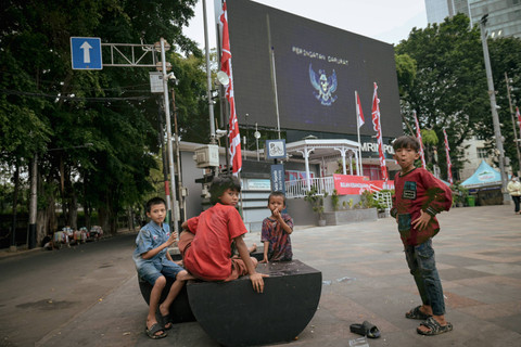 Foto multiple exposure antara sejumlah bocah yang bermain di kawasan Bundaran HI dengan seruan Peringatan Darurat di ruang publik. Foto: Jamal Ramadhan/kumparan